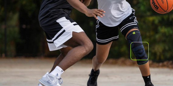 Volle Kontrolle – mit jedem Schritt sicher am Ball Zwei Basketballspieler auf einem Außenplatz im Spiel. Die im Vordergrund agierende Spielerin trägt eine schwarze Kniebandage und dribbelt den Ball, während sie von einem Gegenspieler verteidigt wird.