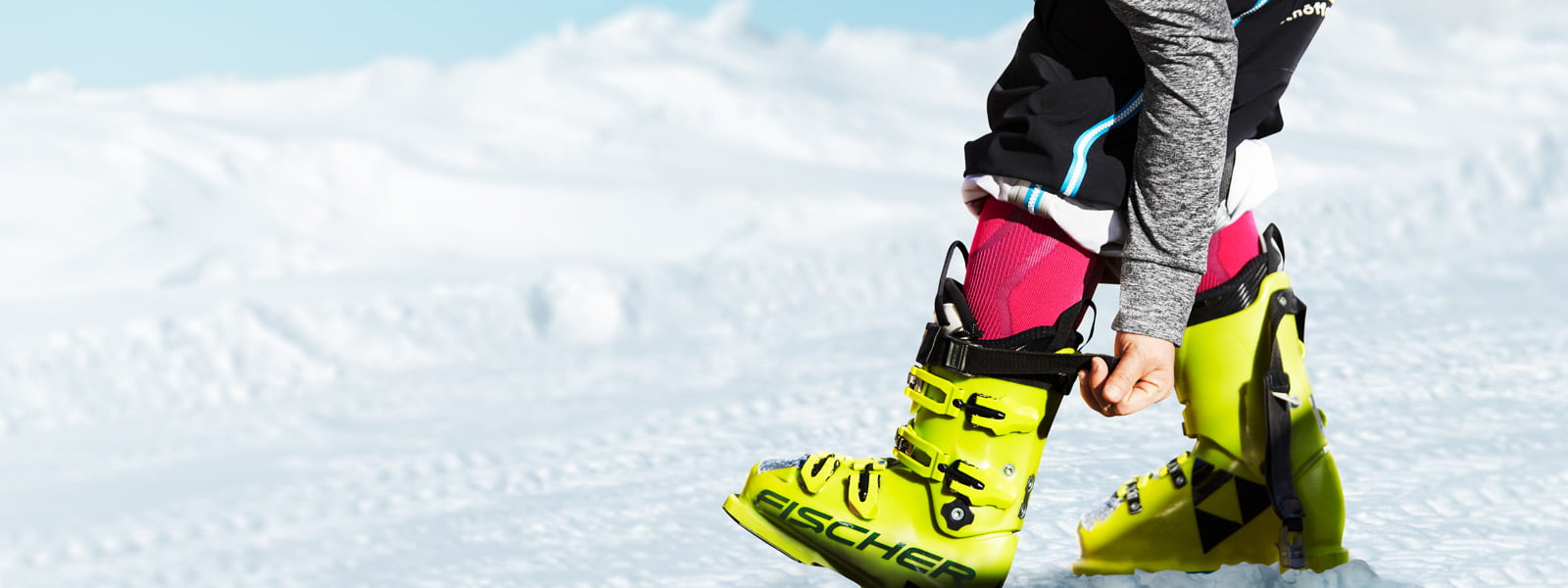Les Ski Performance Compression Socks roses juste avant le plaisir sur les pistes Skieur avec des chaussettes de ski roses et une manche grise serre la sangle de sa chaussure de ski jaune en arrière-plan neige