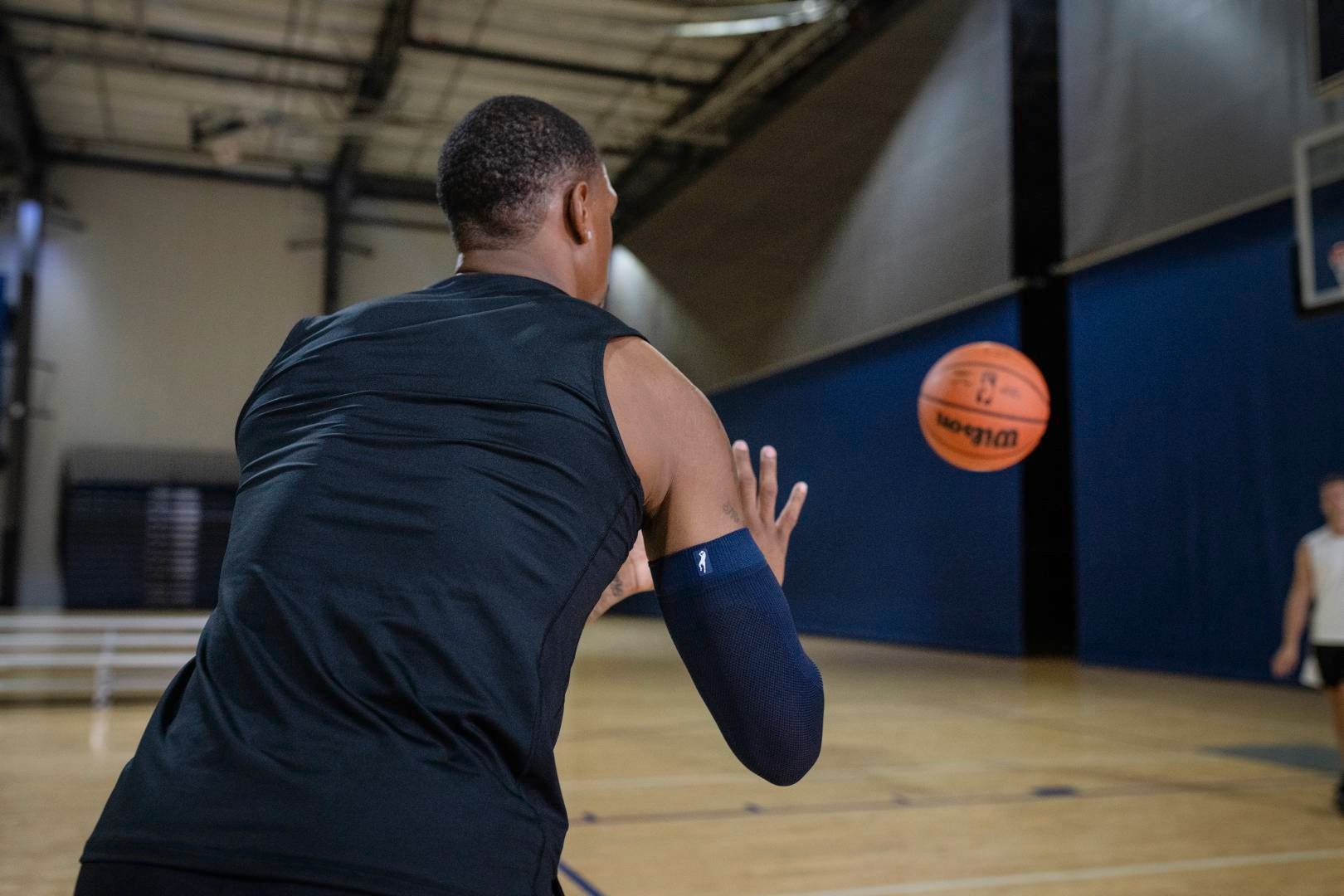 Joueur de basketball avec une manche bleue en salle de sport attend un ballon qui lui est lancé par un autre joueur