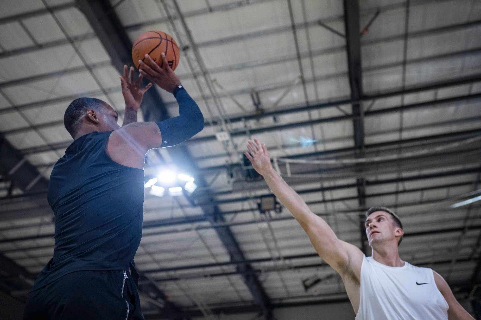 Joueur de basketball avec un manchon bleu au bras dans un gymnase tente de lancer par-dessus le bras tendu d'un adversaire