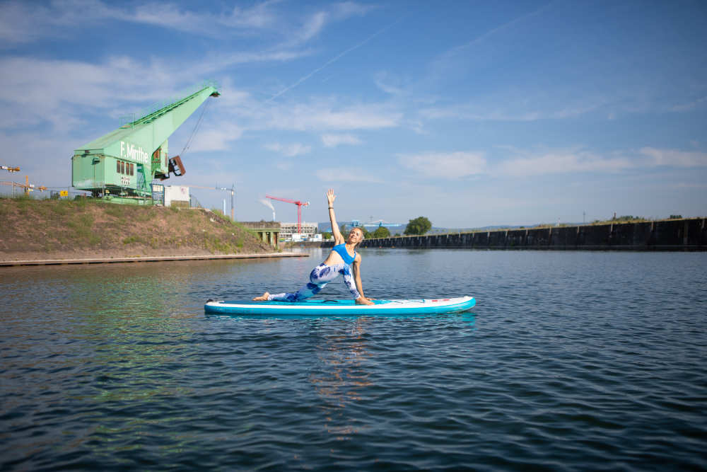SUP Yoga - se laisser simplement flotter Femme fait un exercice de yoga sur la planche avec des grues en arrière-plan