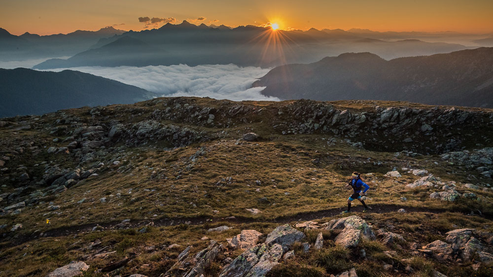 Ultrarunner auf einem Bergtrail bei Sonnenaufgang mit Blick über die Alpen