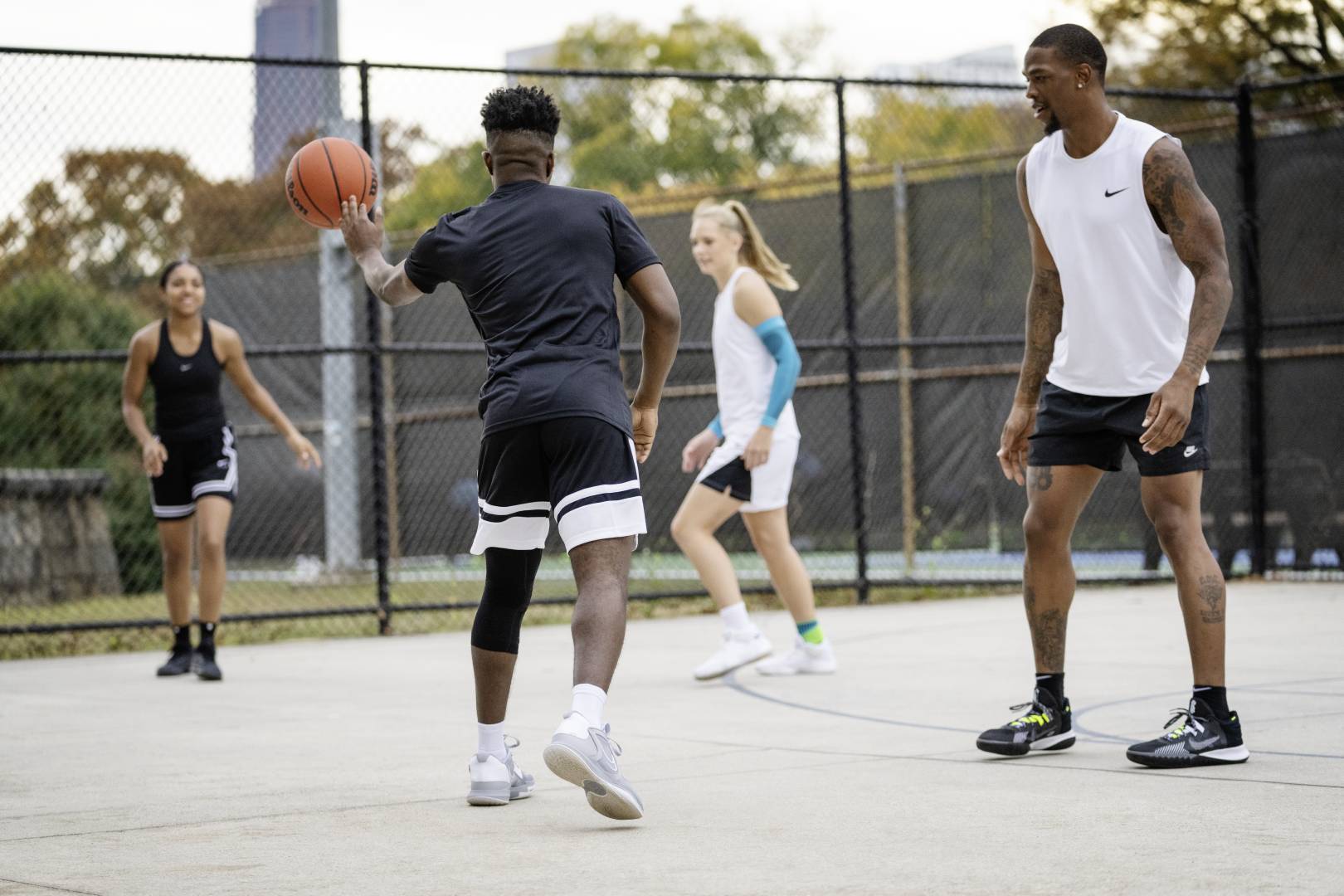 un joueur de basketball passe à une joueuse Quatre joueurs/joueuses pendant un match de streetball, le joueur en tenue de jeu noire passe le ballon à sa coéquipière