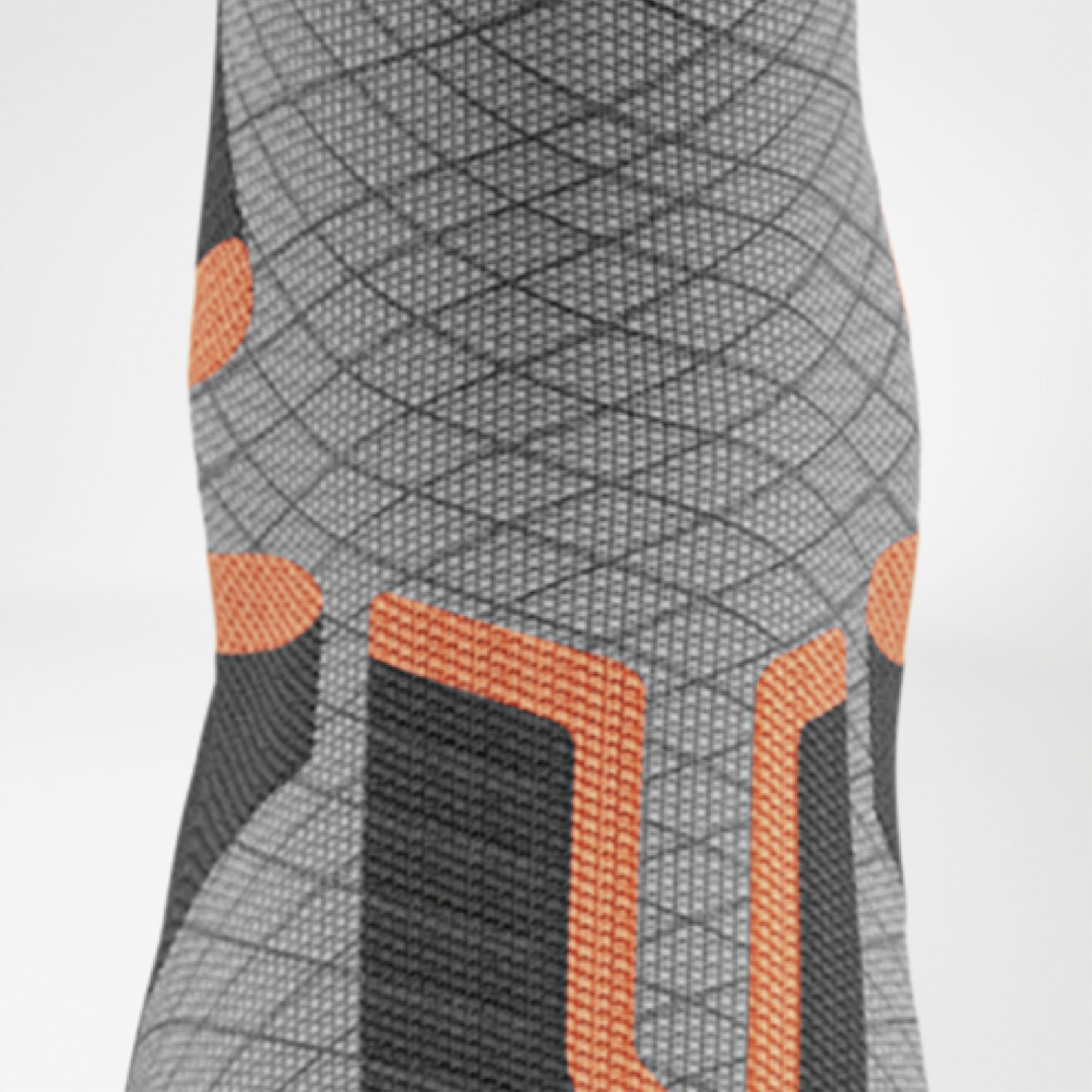 Frontale Nahaufnahme der Ski-Kompressionssocke im Schienbeinbereich mit U-förmiger orangefarbener Polsterung und rautenförmiger Strickstruktur für gezielten Schutz.