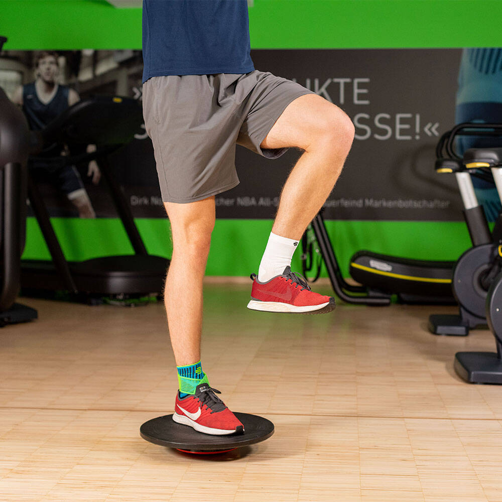 Un Balance Pad est un excellent moyen d'améliorer votre coordination et votre équilibre Homme dans une salle de sport en équilibre sur une jambe droite avec un Balance Pad, portant une chevillère