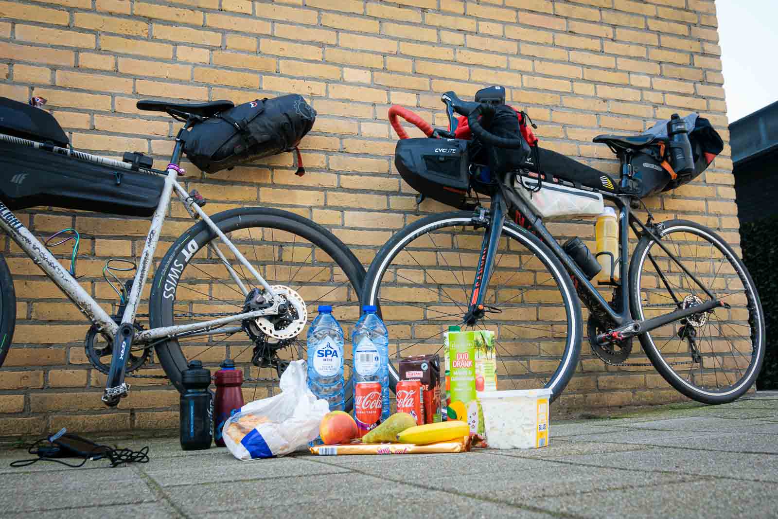 Aliments sur le sol devant deux vélos Sur le sol se trouvent des provisions de deux participants de la Race around the Netherlands, y compris de l'eau, du cacao, de la salade de pommes de terre et du coca