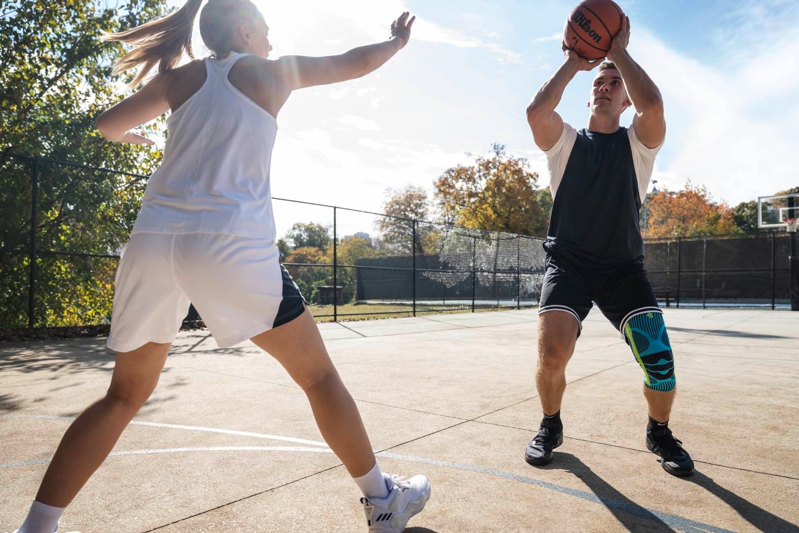 Un joueur de basketball avec une genouillère tente un lancer en streetball tandis que son adversaire essaie de le bloquer