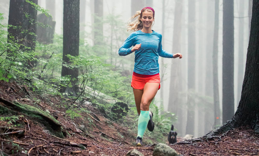 Femme marche avec des chaussettes de Outdoor longues et avec un chien sur un chemin forestier