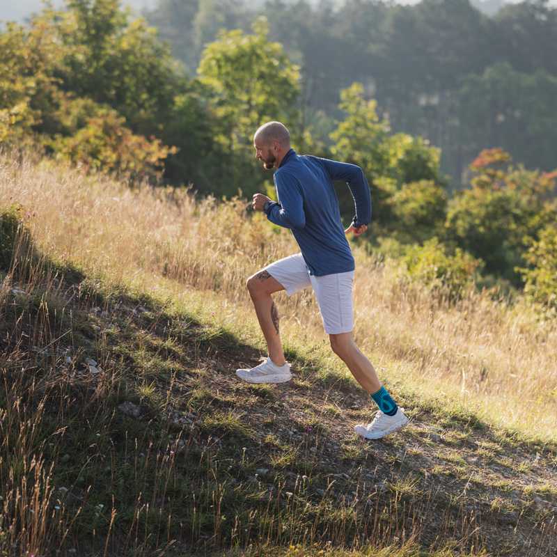 Mehr Sicherheit in jedem Gelände mit der Bauerfeind Sports Achilles Support Mann rennt mit einer Achillessehnenbandage am Fuß einen Hügel mit Gras hinauf