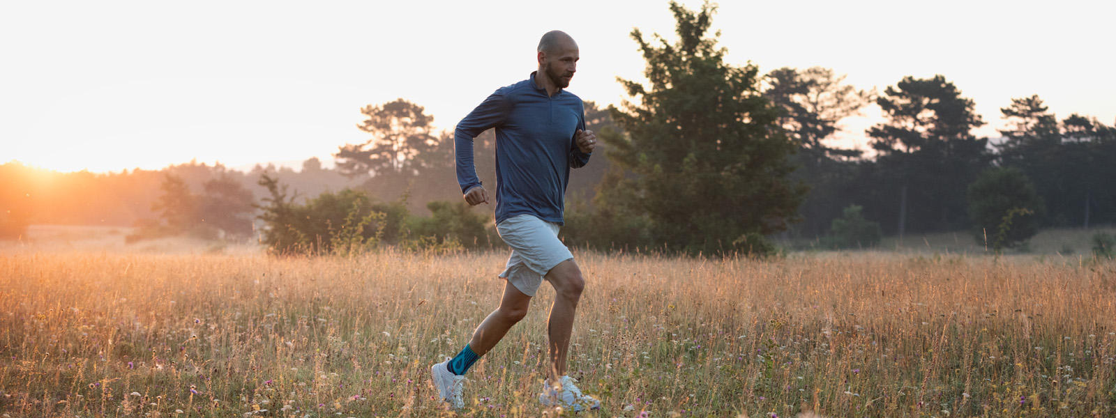 Dire adieu aux douleurs du tendon d'Achille en courant - avec notre Sports Achilles Support Homme avec une chevillière court au crépuscule à travers une prairie à herbes hautes