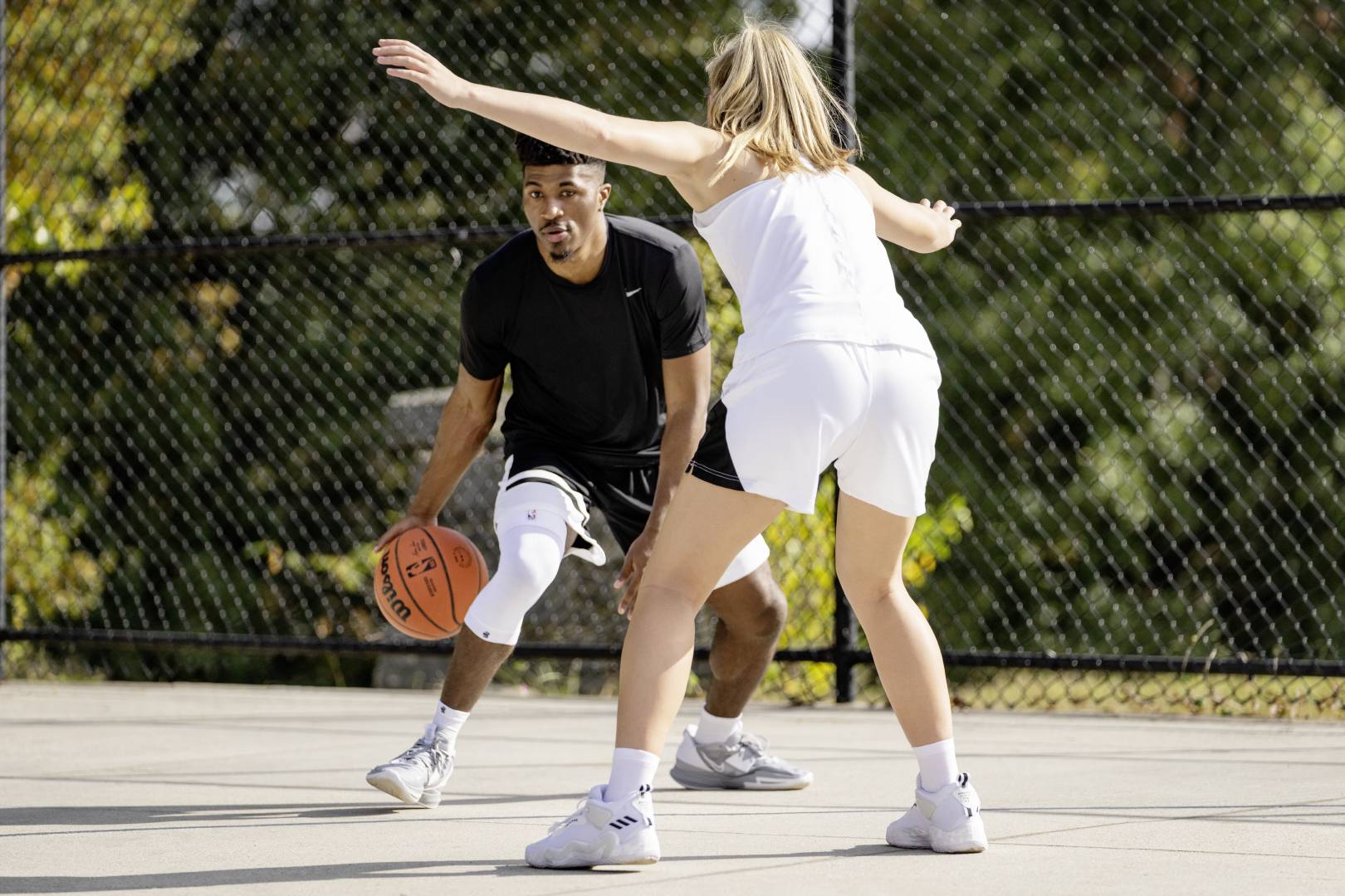 Joueur de streetball avec un Knee Sleeve blanc en duel Joueur de streetball avec un Knee Sleeve blanc essaie de passer une adversaire en driblant, qui l'attend avec les bras écartés