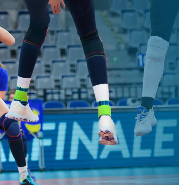 Pour un atterrissage en douceur : Notre Sports Ankle Support au volleyball Joueuse de volley-ball avec un pantalon sombre, des chaussures blanches et des bandages de cheville bleus "suspendue" en l'air
