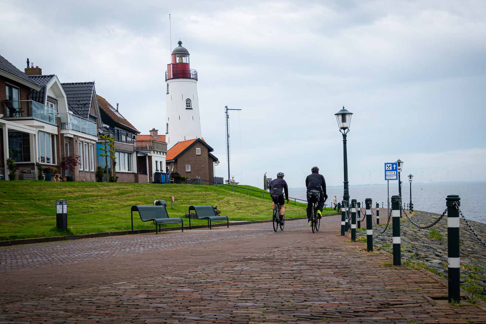 Ultra-Cycling Radfahrer an einer Promenade mit Leuchtturm Zwei Ultra-Cycling Radfahrer von hinten die eine Promenade entlang fahren wo ein Leuchtturm steht.