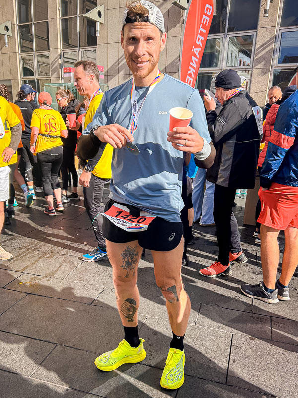 Im Ziel nach dem Halbmarathon in Halle, stolz mit Medaille und Getränk Stolz nach dem erfolgreichen Halbmarathon in Halle stehend, mit Medaille und Getränk in der Hand, den Moment nach dem Rennen genießend.