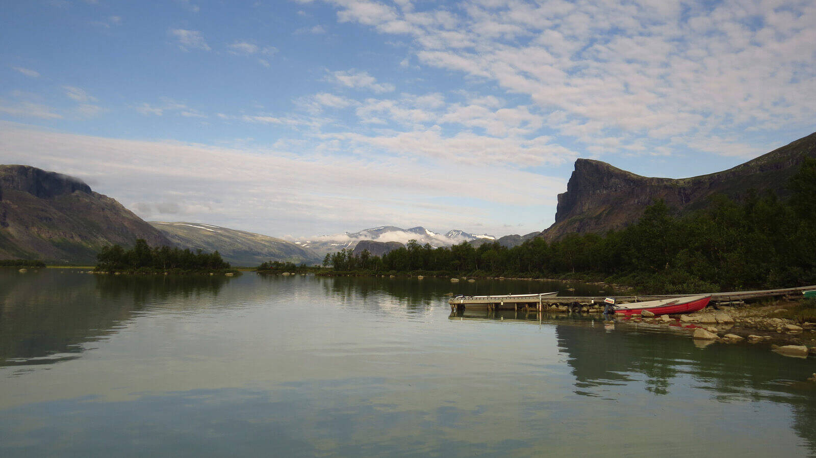 Le Kungsleden n'est pas considéré comme l'un des sentiers de randonnée les plus populaires en Europe sans raison. Panorama d'un lac entouré d'arbres et de petites montagnes. À droite, un petit bateau est amarré au quai.