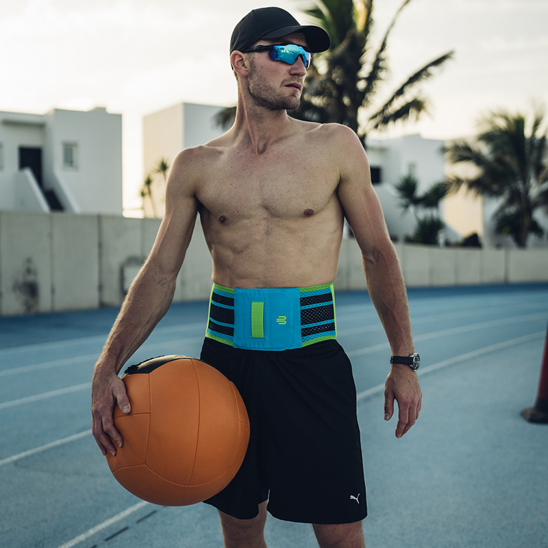 Même à la plage un attrait: notre Sports Back Support Femme portant une attelle dorsale bleu-vert en été devant un décor rocheux