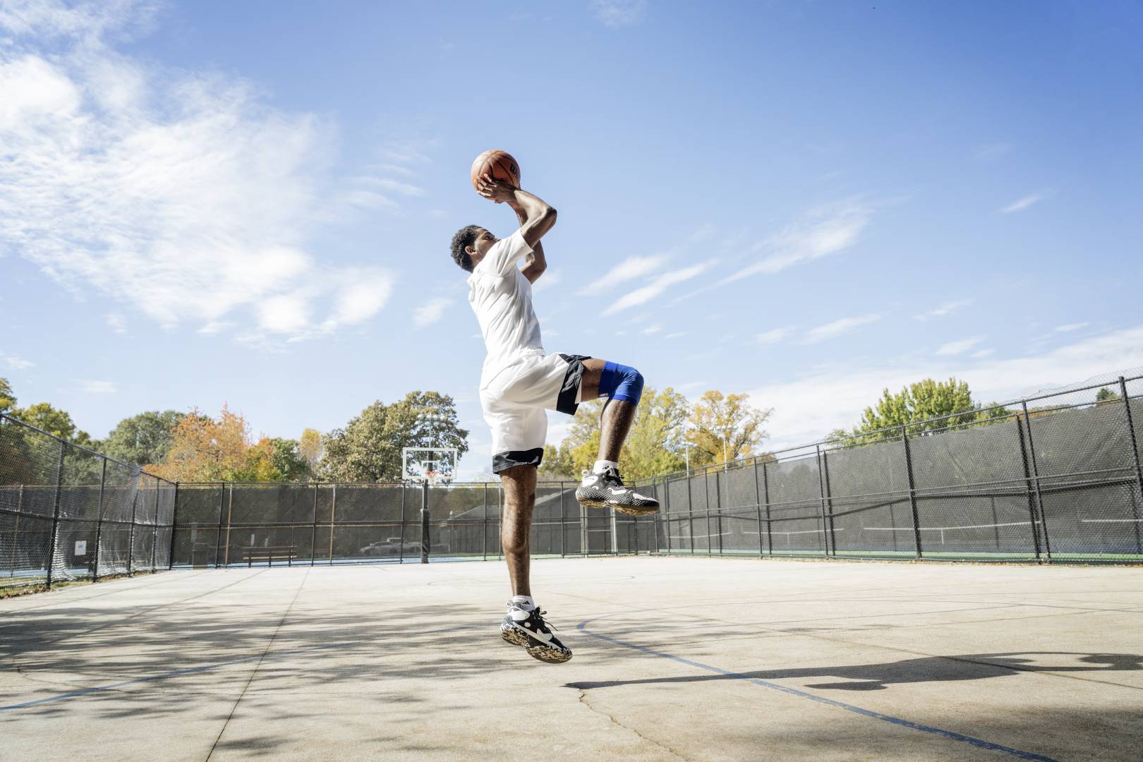 Le basketteur saute et porte une genouillère Le basketteur saute sur un terrain de rue pour le tir, les mains avec le ballon au-dessus de la tête, une jambe fléchie, l'autre pointant verticalement vers le bas