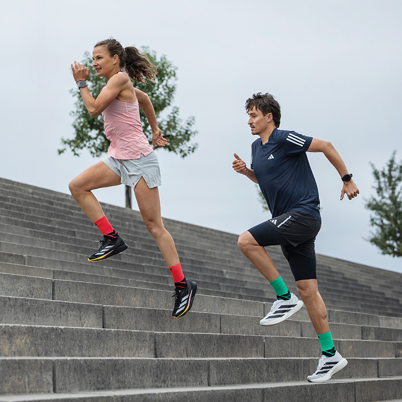 Les sœurs Hahner adorent mettre les gaz - et donc aussi les Run Performance Compression Socks Deux femmes courent énergiquement dans une rue de la vieille ville avec de petits balcons