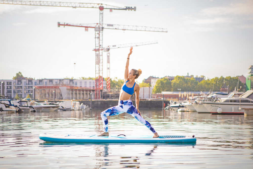 Le SUP Yoga est idéal pour l'été Femme fait du yoga sur une planche avec un port en arrière-plan